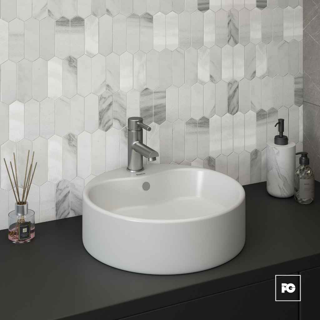 Round white vessel sink with a modern silver faucet on a dark countertop, marble hex tile backsplash, with diffuser and soap dispensers nearby.